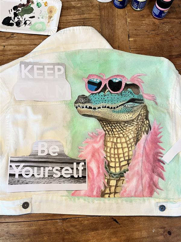 Jana Menzi's hand-painted denim jacket featuring a crocodile with pink sunglasses and feather boa against an Everglades landscape